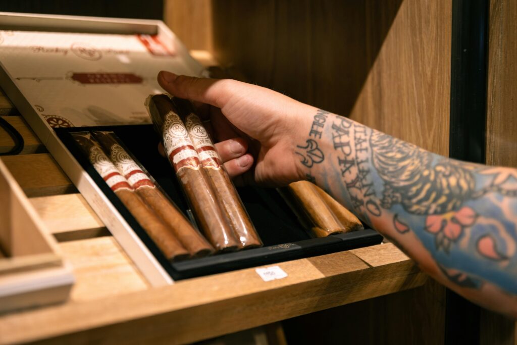 tattooed person reaching for cigar out of cigar humidor